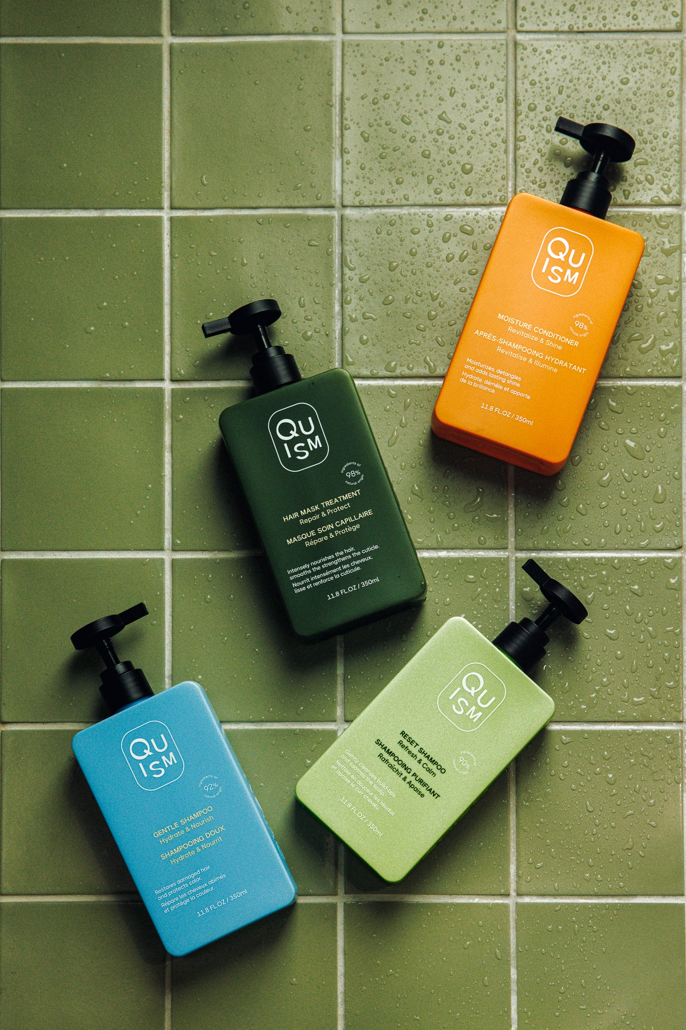 Five bottles of Quism haircare products on a green tiled surface